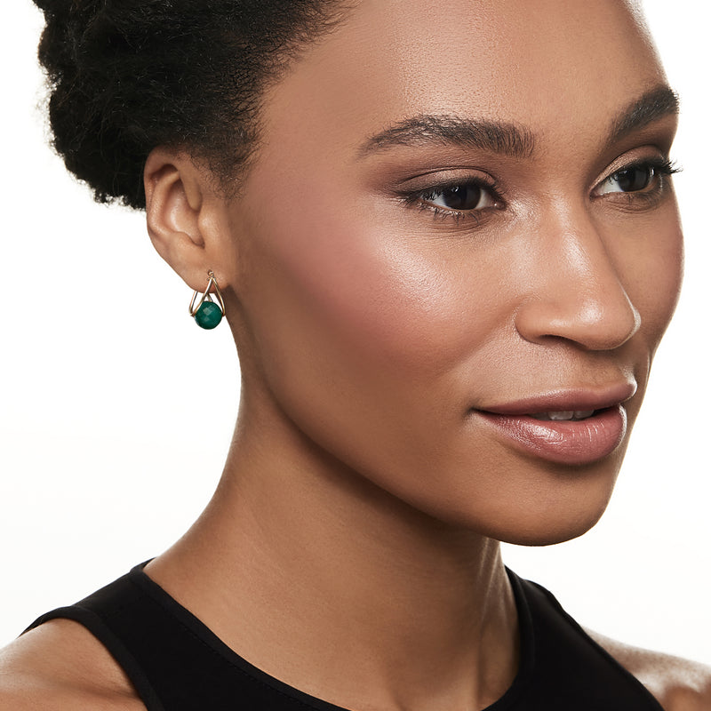 Model wearing gold double-hoop earrings with emerald green teardrop bead