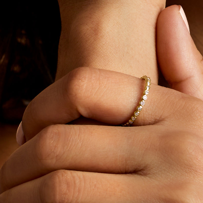 Yellow gold diamond eternity band with bezel-set round stones on finger