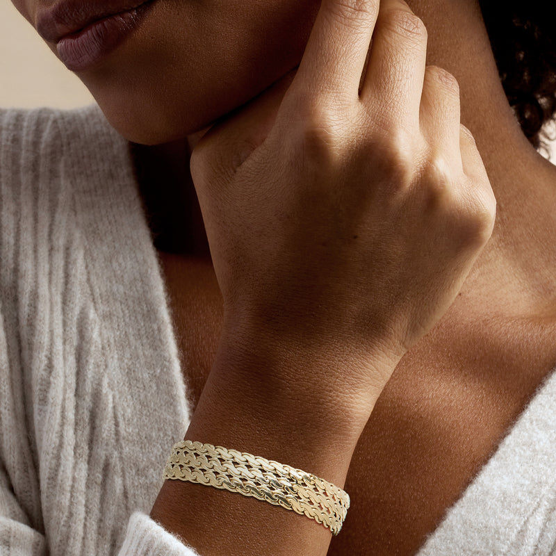 Serpentine-link yellow gold bracelet worn on wrist, three-row design.