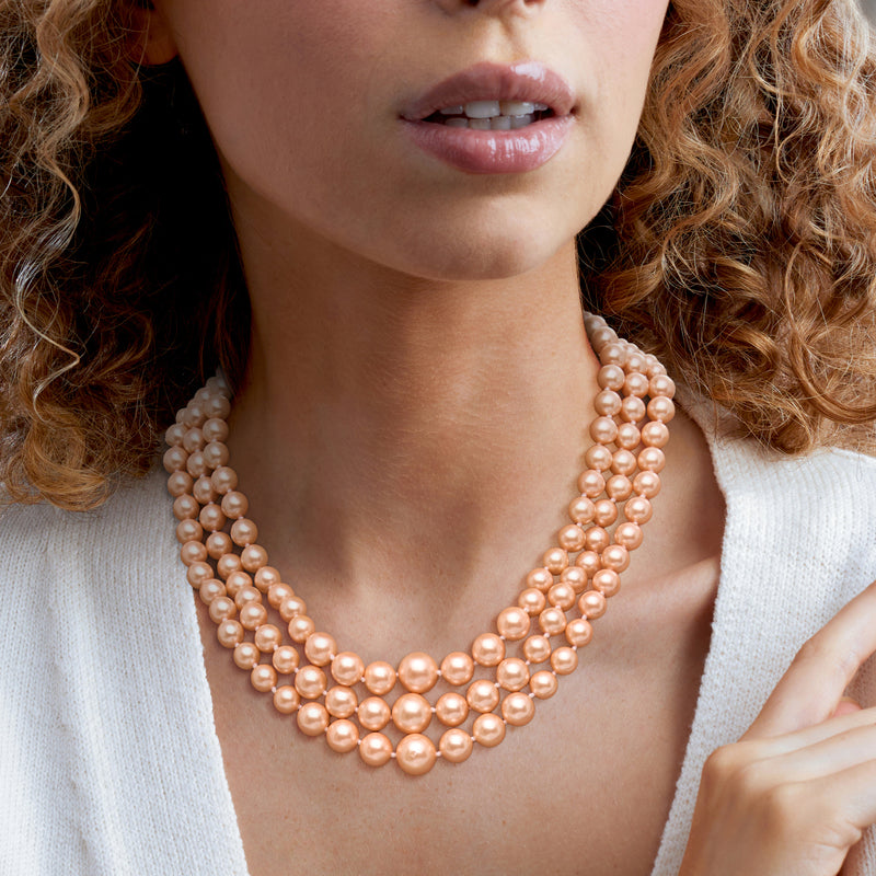 Peach shell pearl three-strand necklace worn at the collar, graduated pearl rows
