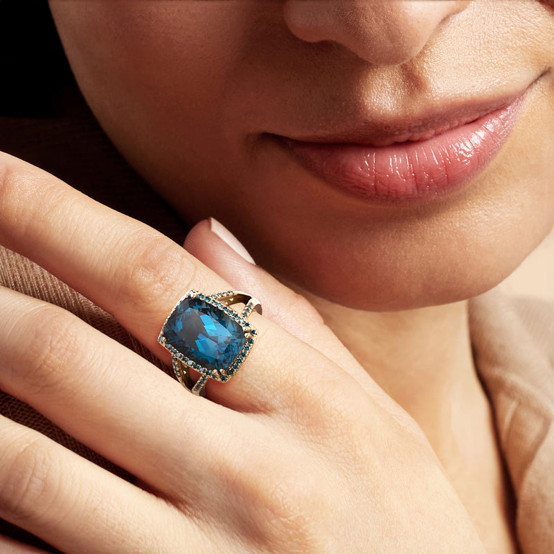 Blue gemstone ring with diamond halo on finger, 14kt yellow gold band