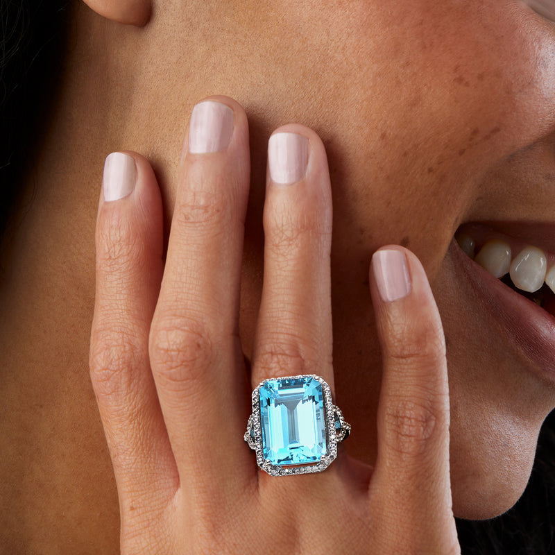 Sterling silver ring with rectangular blue topaz on finger, halo and side white topaz