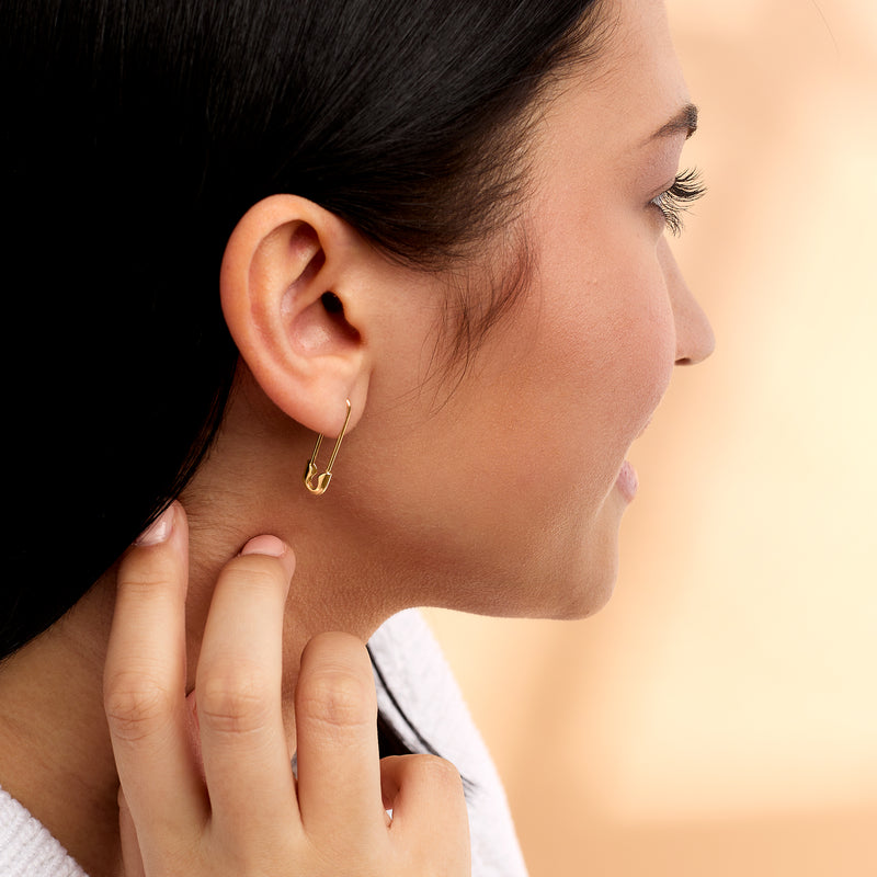 Model wearing 14kt yellow gold safety pin earrings with small pin drop on ear