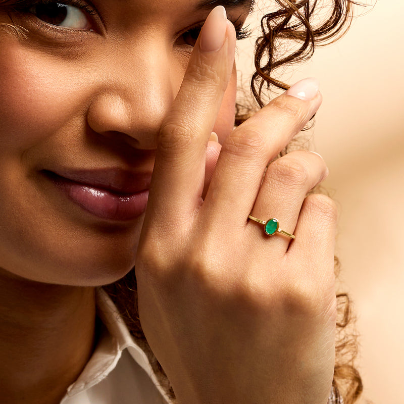 Yellow gold emerald ring on finger with oval green stone and thin band
