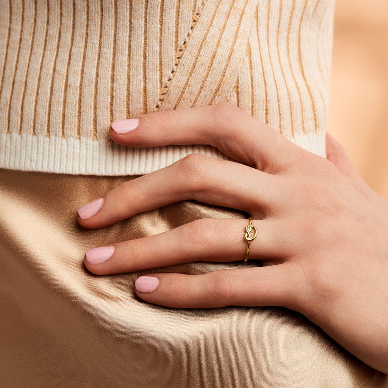 Yellow gold love-knot ring on finger, polished slim band