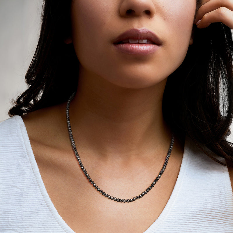Black diamond bead necklace worn at the neckline with dark round bead strands