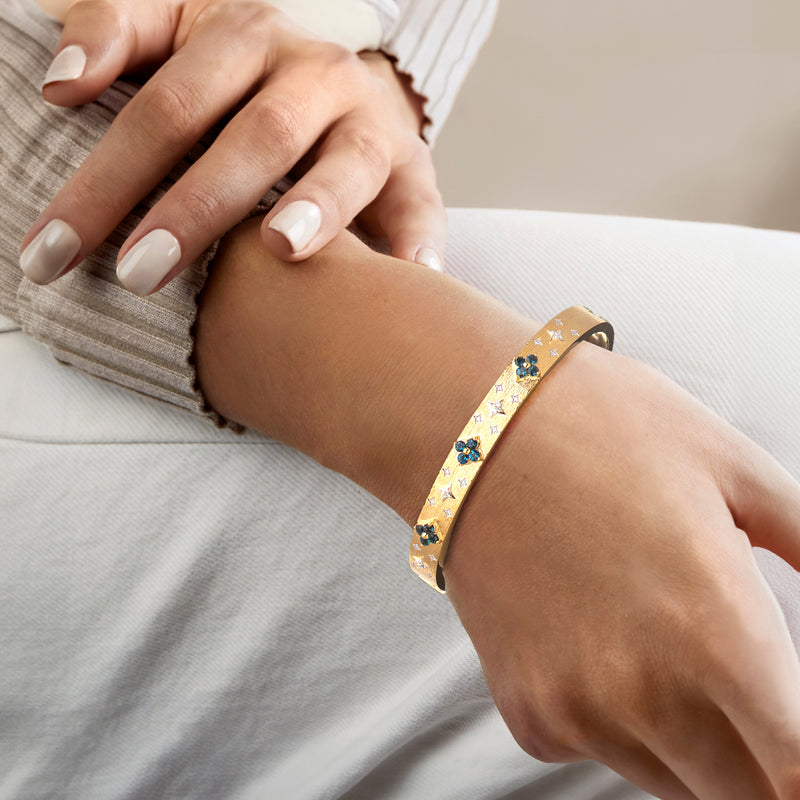 Gold topaz bangle on wrist with blue floral settings and diamond accents