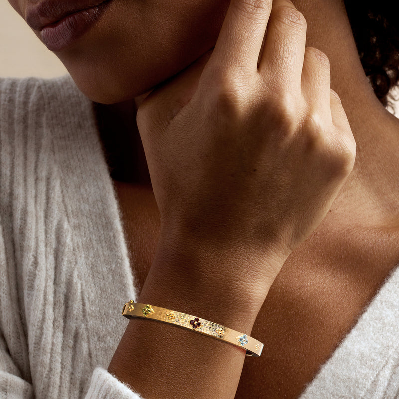 Gold floral bangle bracelet worn on wrist with small red and blue gemstone flowers
