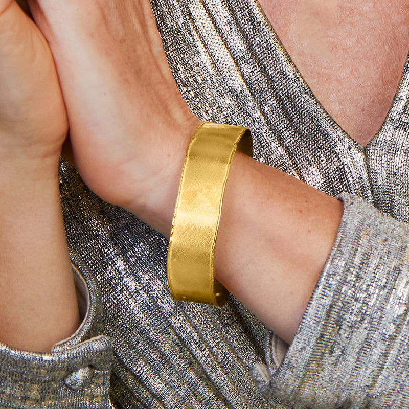 Gold-tone cuff bracelet on wrist, smooth wide band with open ends