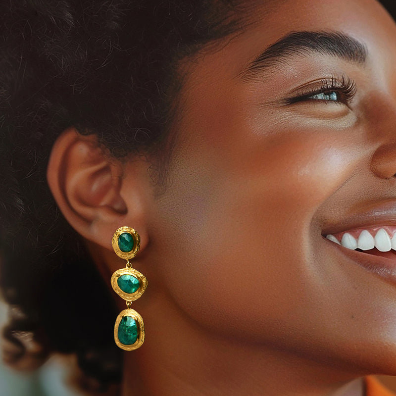 Gold drop earrings with three oval green gemstones, worn on the ear