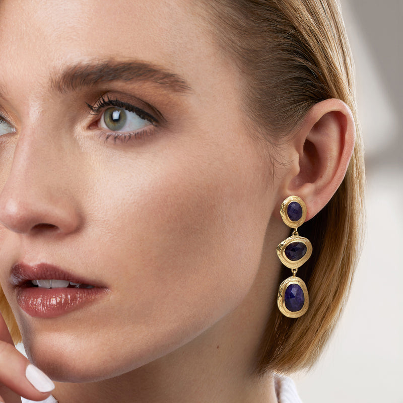 Gold drop earrings on model: three oval deep-blue sapphire stones