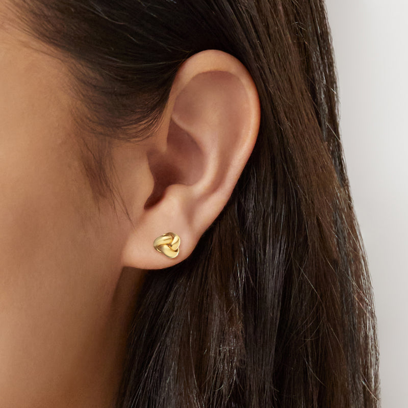 Yellow gold love knot stud earrings shown on ear