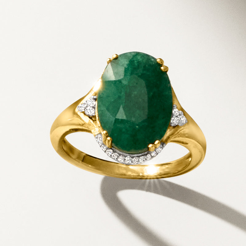 Gold oval emerald ring with diamond trim around green center stone and curved band