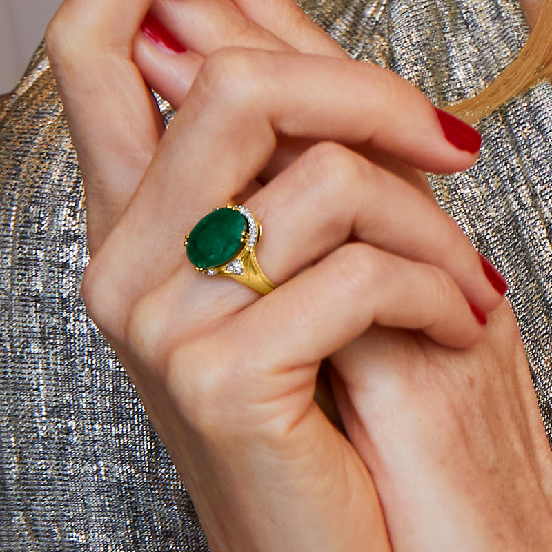 Emerald-green oval ring on finger with diamond halo and gold prongs