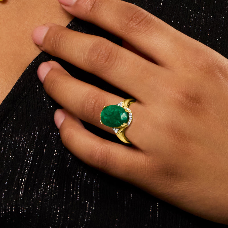 Emerald-green oval gemstone ring on finger with diamond halo set in gold
