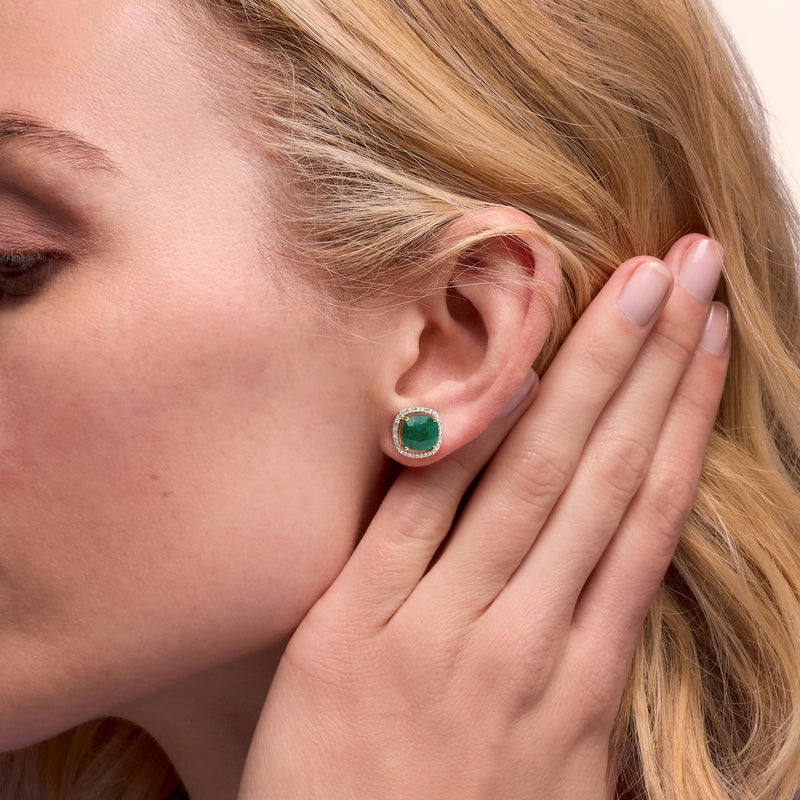 Emerald stud earrings with round halo diamonds and gold bezel, worn as posts