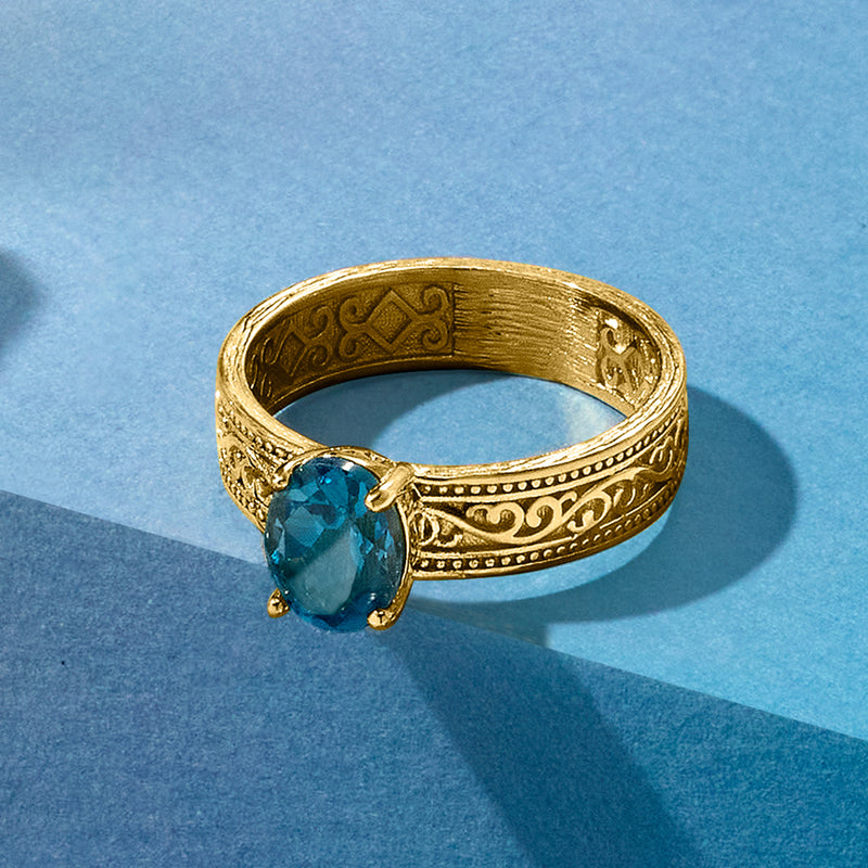 Gold-tone ring with oval blue topaz set in ornate scrollwork band