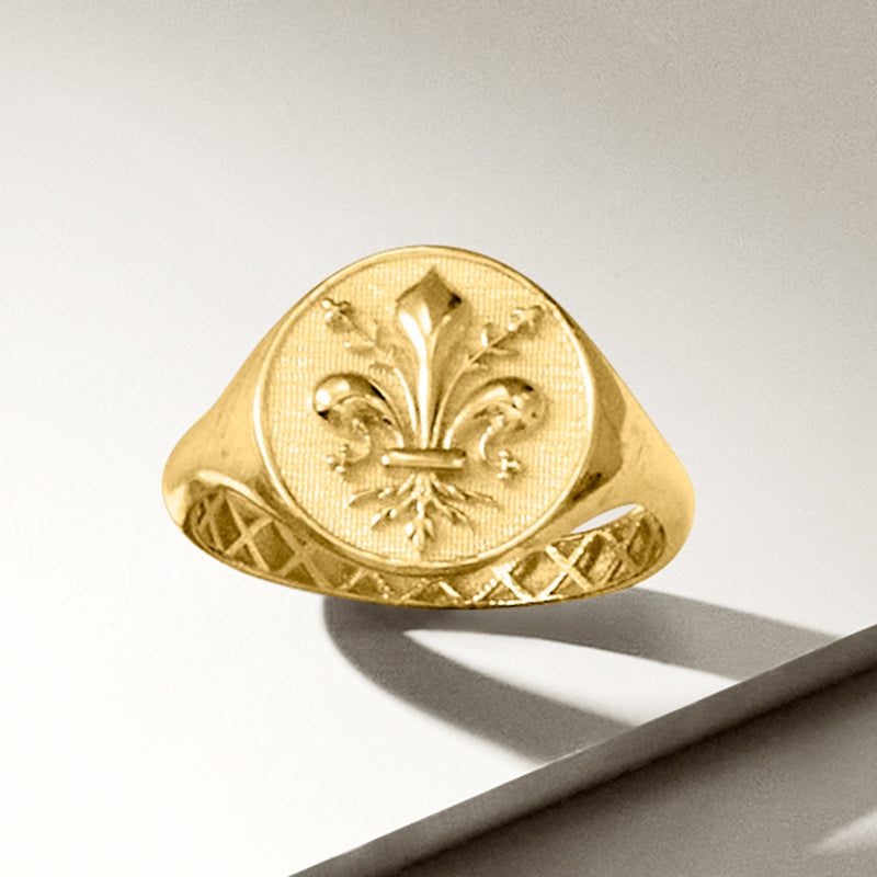 Yellow gold fleur-de-lis signet ring, angled view showing engraved band texture