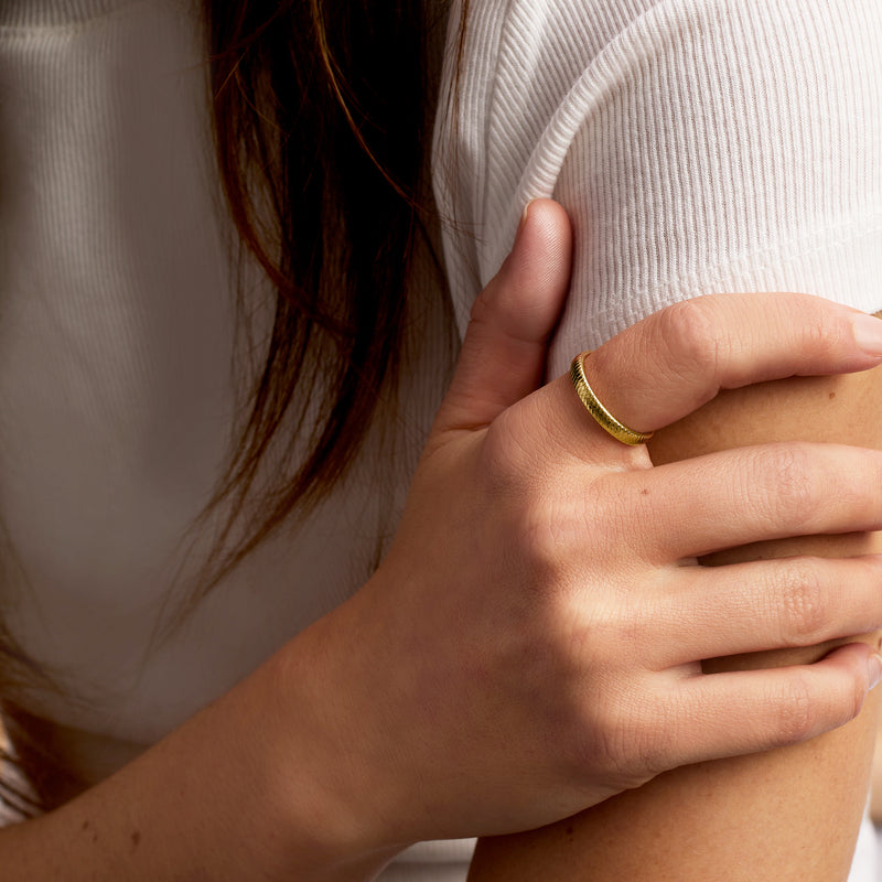 Yellow gold textured band ring on finger, snake-scale ridged surface