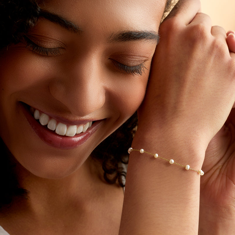 Cultured pearl station bracelet on wrist, small white pearls in 14kt yellow gold