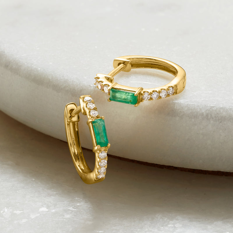 Yellow gold huggie hoop earrings with green emerald center and diamond halo accents