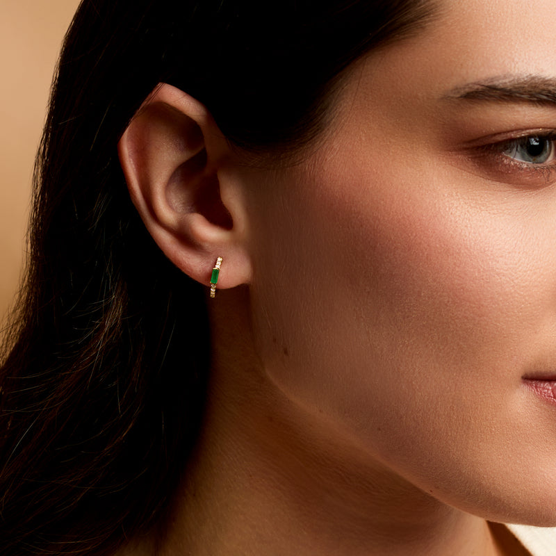 Huggie hoop earrings on ear: yellow gold hoops with green emerald and small diamonds