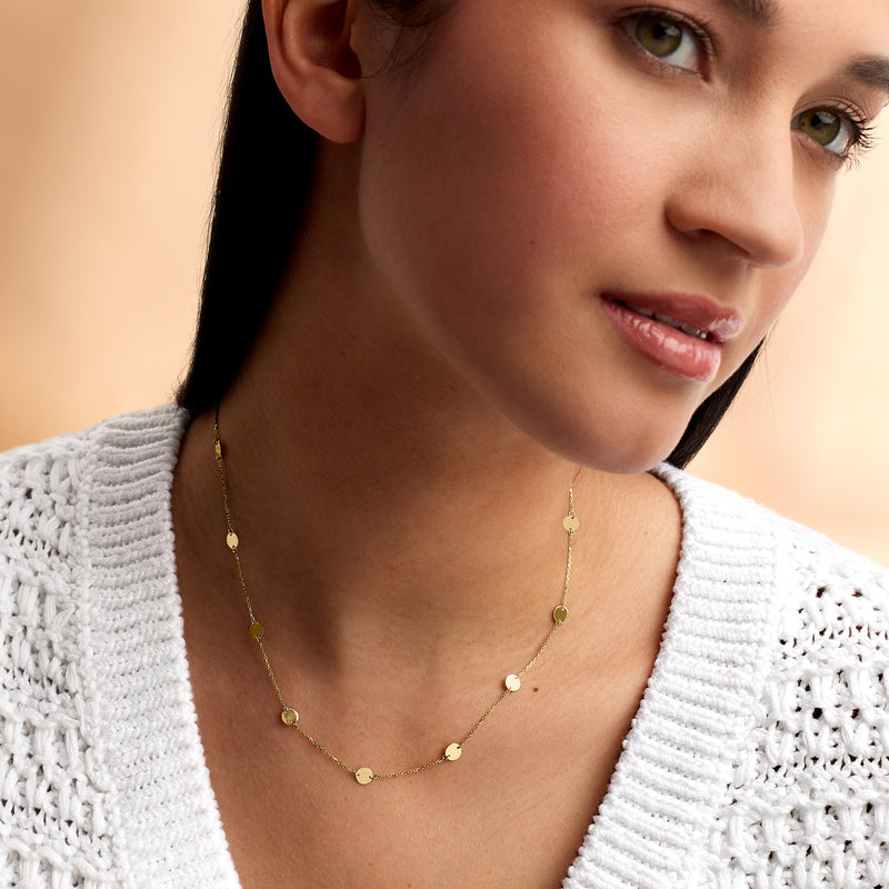 Yellow gold disc station necklace with small round disc charms, close-up at neckline
