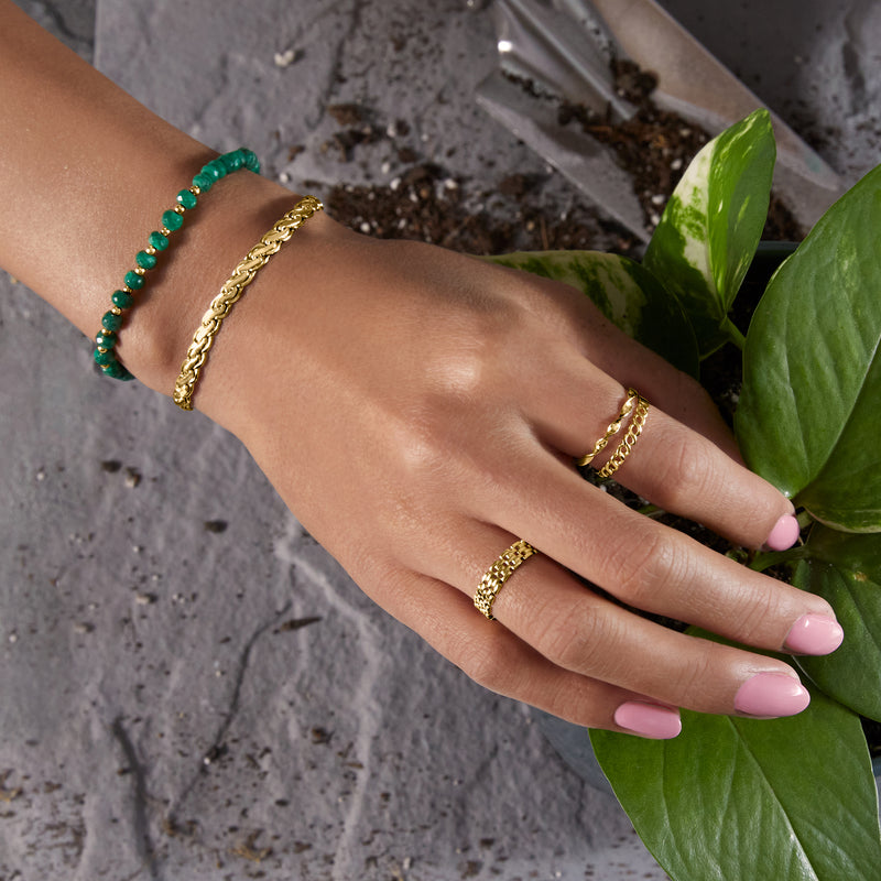 10kt yellow gold curved-link bracelet on hand, stacked with green beaded bracelet