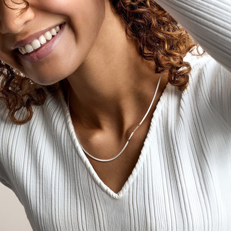 Sterling silver herringbone chain necklace on model with V-neck ribbed shirt