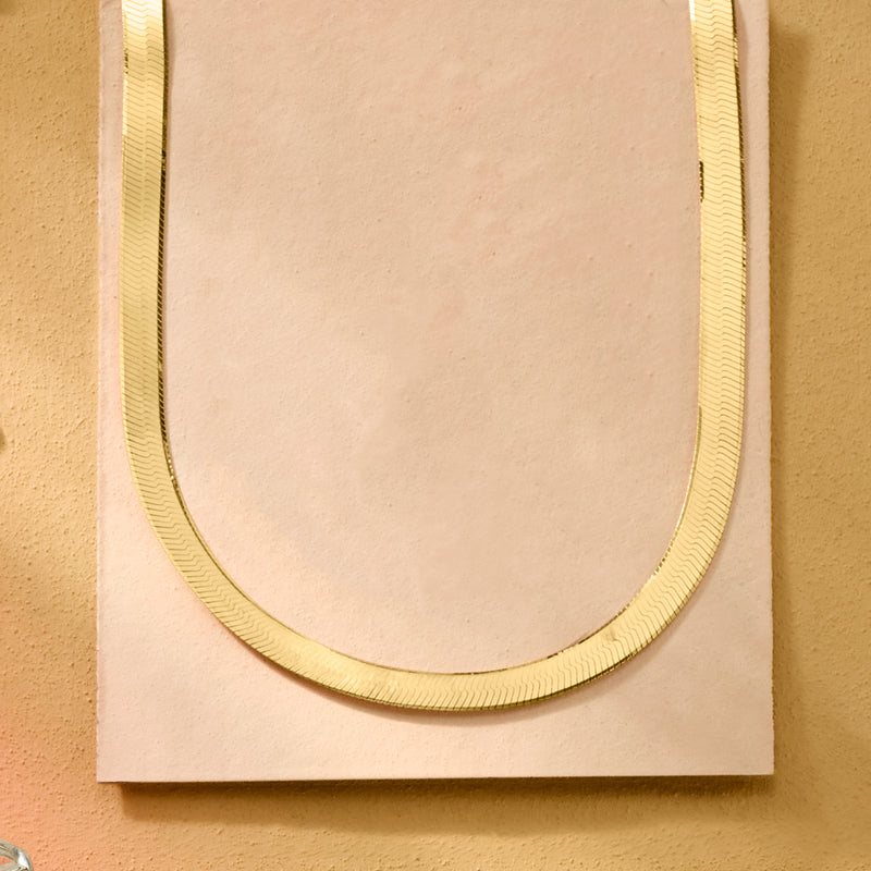 Gold-tone herringbone chain necklace on display card, curved close-up