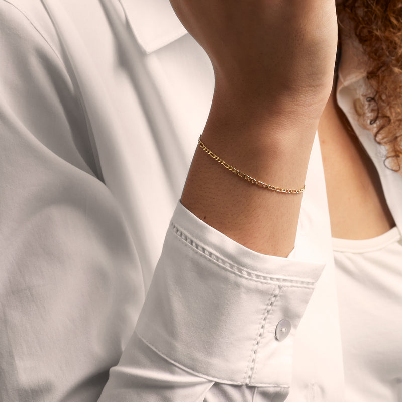Figaro-link gold bracelet on wrist with small chain links