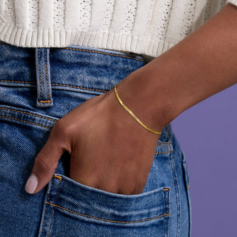 Yellow gold herringbone bracelet on wrist over blue denim, slim chain