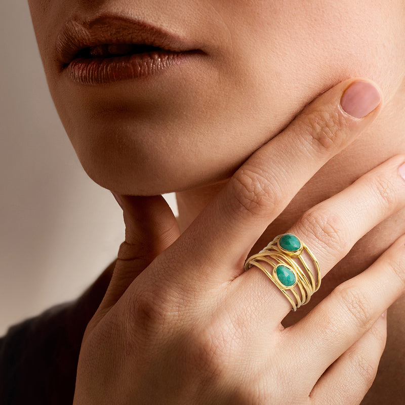 Gold wrap ring with oval green gemstones on finger, stacked braided bands