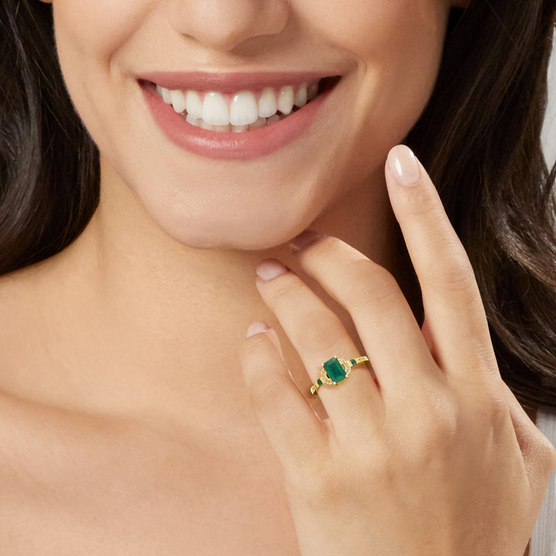 Emerald and diamond ring on finger, square green center stone in yellow gold band