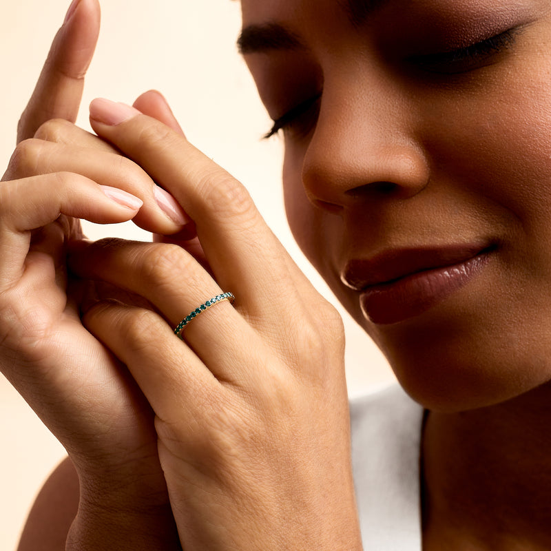 Hand wearing 14kt yellow gold ring with London blue topaz stones, slim band