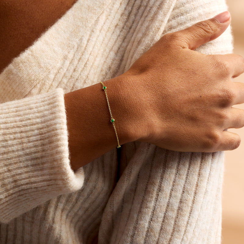 14kt yellow gold station bracelet on wrist with small emerald green round stones