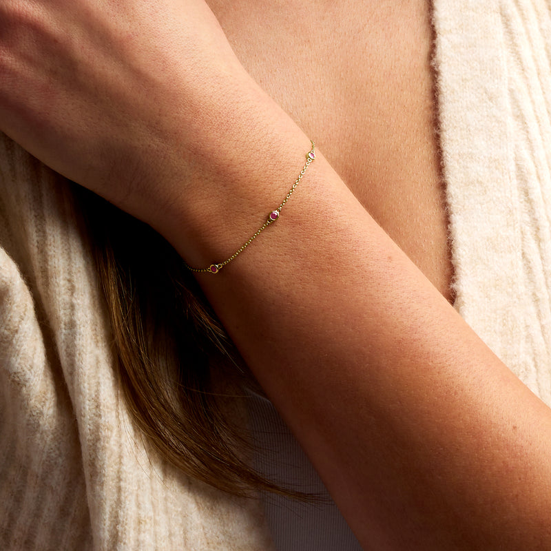 Ruby station bracelet in 14kt yellow gold with small pink round stones, worn on wrist