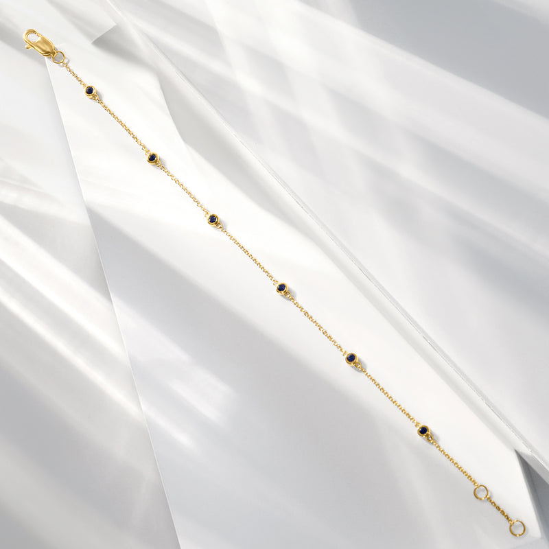 Gold station bracelet with small round blue gemstones along the chain