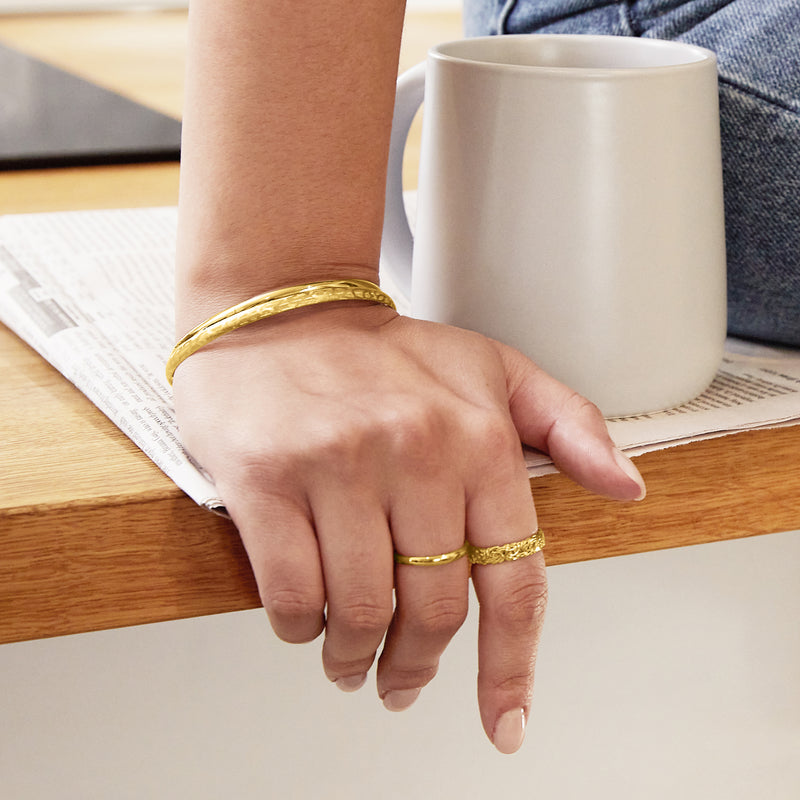 Yellow gold bangle bracelet on wrist with hinged clasp and brushed finish