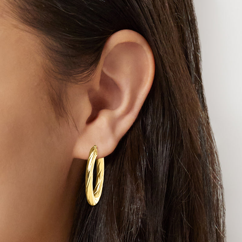 Twisted oval hoop earrings in 10kt yellow gold, worn on ear.