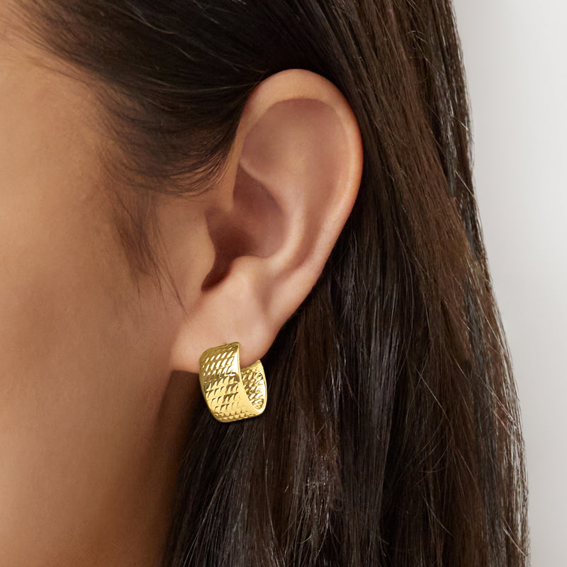 Textured yellow gold huggie hoop earrings on ear, close-up