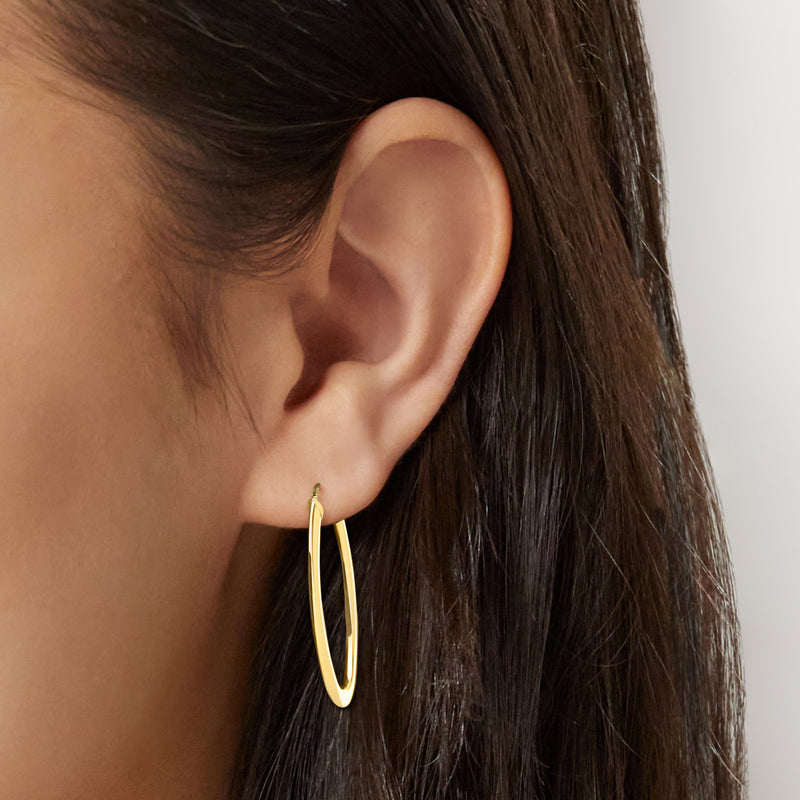 Yellow gold oval hoop earrings worn, close-up on earlobe and hoop shape
