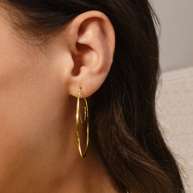 Yellow gold double-hoop hoop earring on ear, polished oval hoops