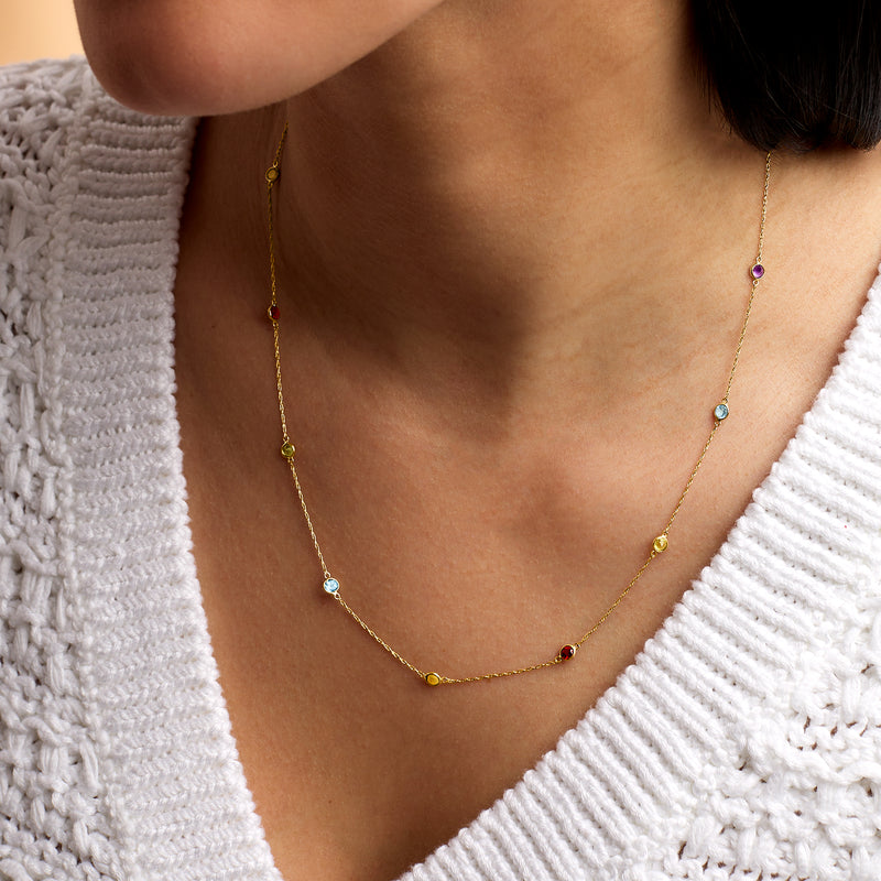 Yellow gold station necklace on neckline with small multicolor gemstones spaced on chain