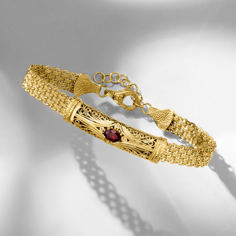 Gold-tone filigree bar bracelet with red garnet accent and textured chain, angled view