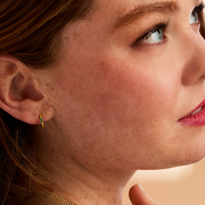 Emerald huggie hoop earrings in 14kt yellow gold, small green stones on wearer