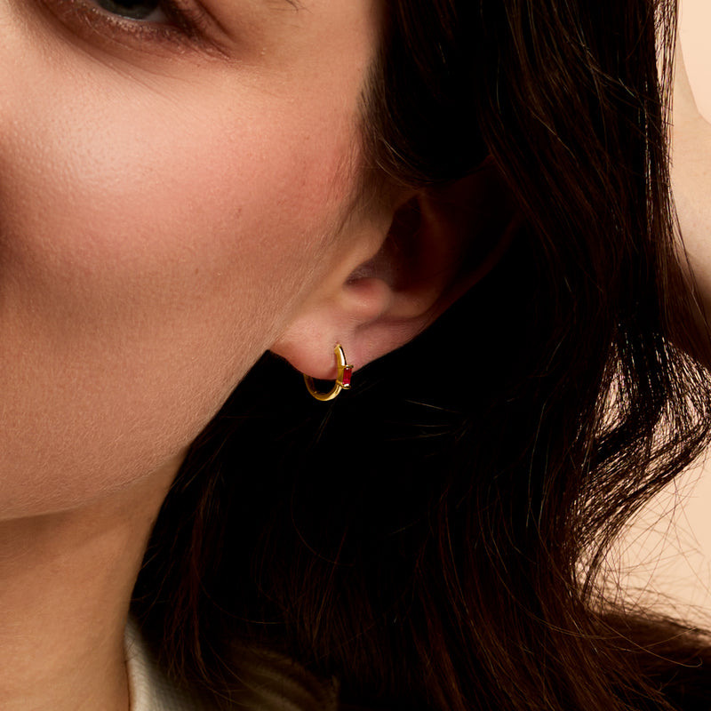 Model wearing 14kt yellow gold ruby huggie hoop earrings with small pink stones