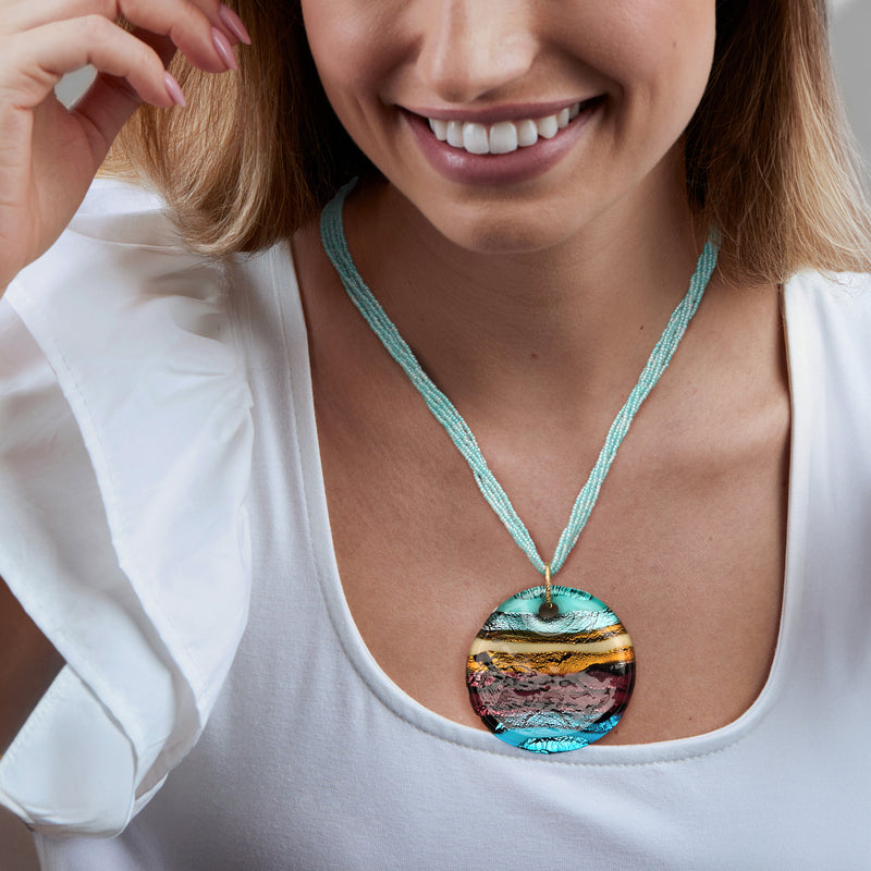 Turquoise beaded necklace with round multicolored glass pendant, worn on neckline