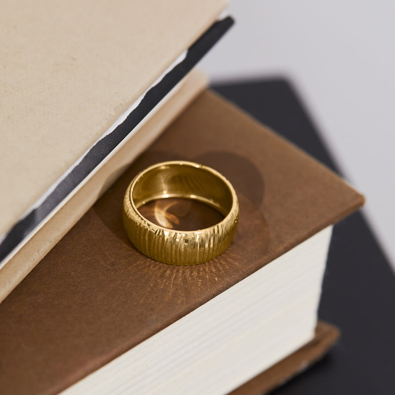 Yellow gold diamond-cut band ring with vertical ridges, shown on a stand