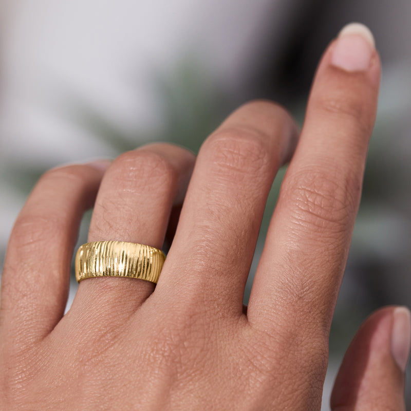 Yellow gold diamond-cut band ring on finger with vertical ridged texture